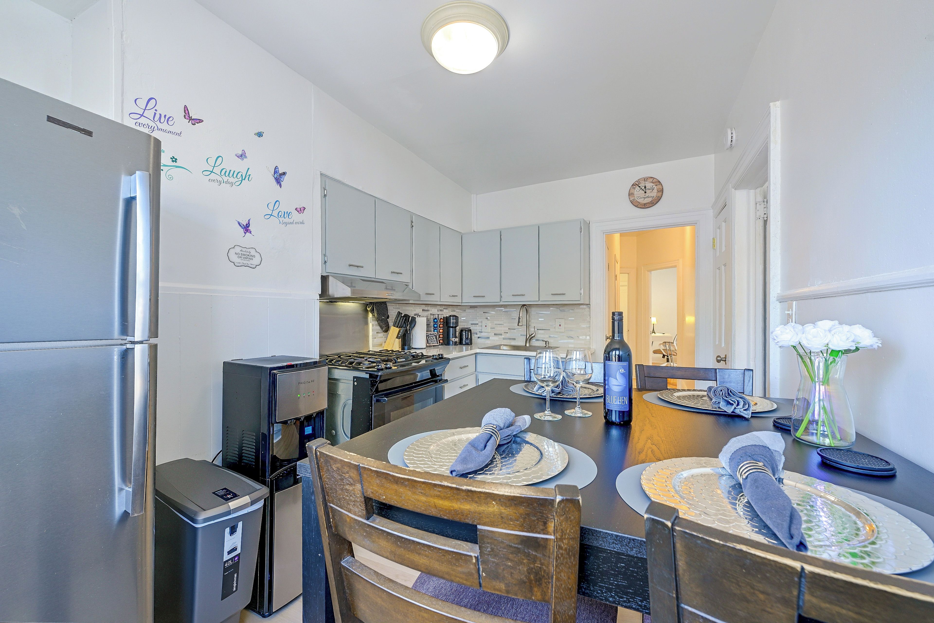A modern kitchen with stainless steel appliances, a dining area with a wooden table and chairs, and decorative wall stickers.