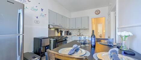 A modern kitchen with stainless steel appliances, a dining area with a wooden table and chairs, and decorative wall stickers.