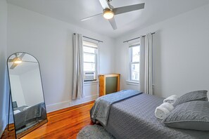 A bedroom with a bed, a ceiling fan, a window with curtains, a mirror, and a radiator.