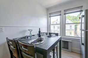 Un coin repas avec une table dressée pour deux personnes, un vase rempli de fleurs et une fenêtre avec des stores.