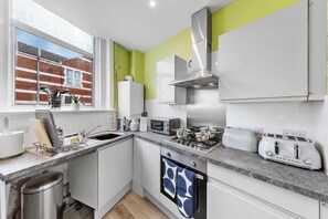 A modern kitchen with a window, stainless steel appliances, and a view of a brick building. - Leyton 1BR Flat | Near Tube, 247 Gym, Tennis Court (Greater London)