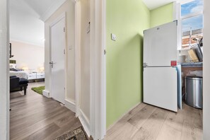 A compact kitchen with a refrigerator, a sink, and a window with a view of the outside. - Leyton 1BR Flat | Near Tube, 247 Gym, Tennis Court (Greater London)
