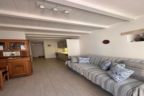 Un soggiorno con un divano, cuscini decorati, un mobile in legno e una cucina sullo sfondo.