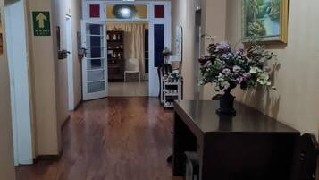 A hallway with a wooden floor, a chandelier, a dining table with chairs, and a painting on the wall.