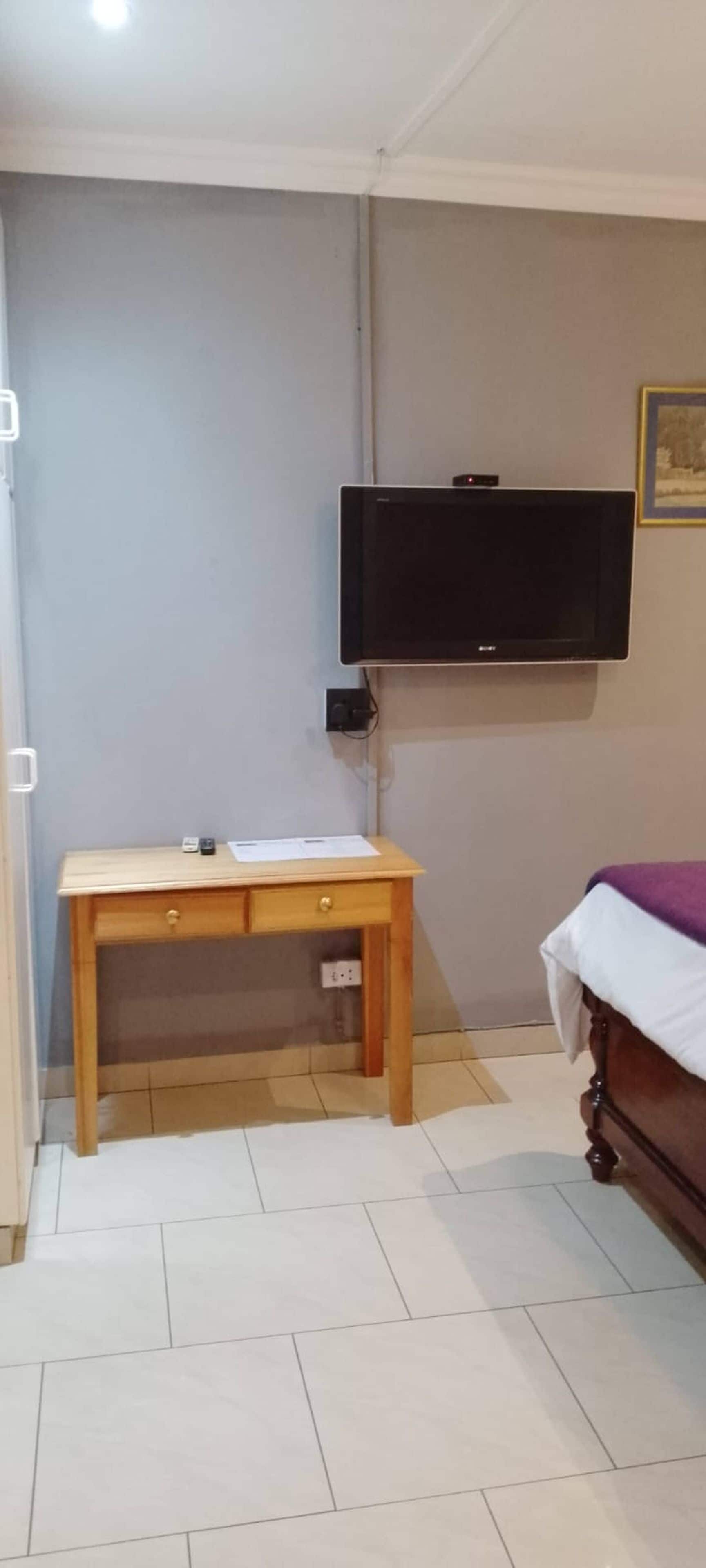 Een kamer met een houten bureau, een bed met een wit en paars deken en een televisie aan de muur.