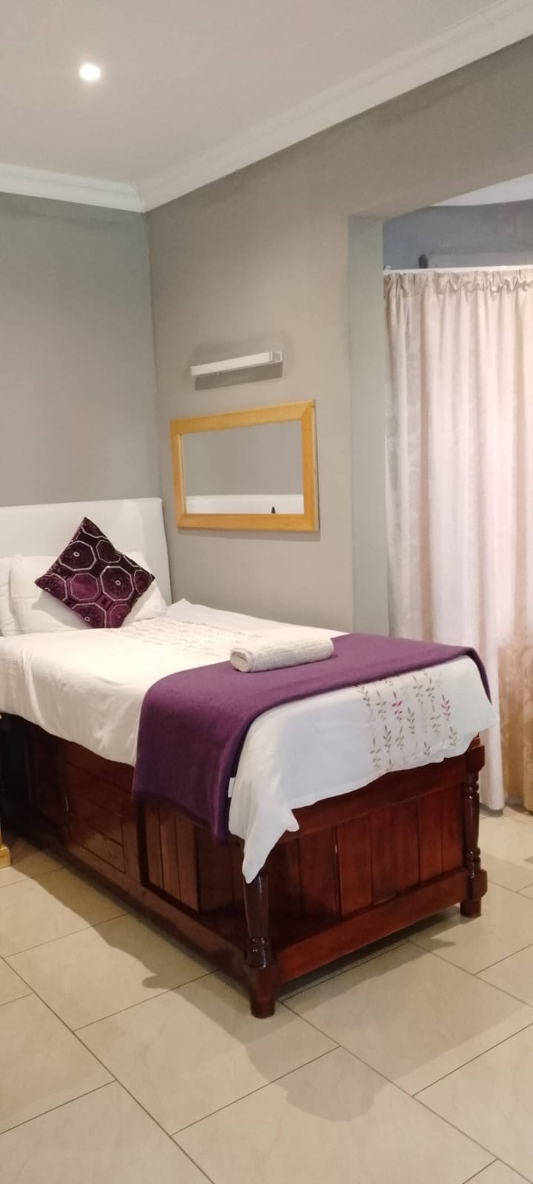 Une chambre à coucher avec un lit, une table de chevet, un miroir et une fenêtre avec des rideaux.