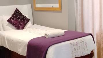 Une chambre à coucher avec un lit, une table de chevet, un miroir et une fenêtre avec des rideaux.