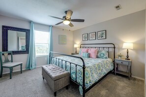 A bedroom with a bed, a chair, a nightstand, a lamp, a ceiling fan, a window with curtains, and wall art. - Perfect Location! Amazing Views & Close to It All! (Branson)