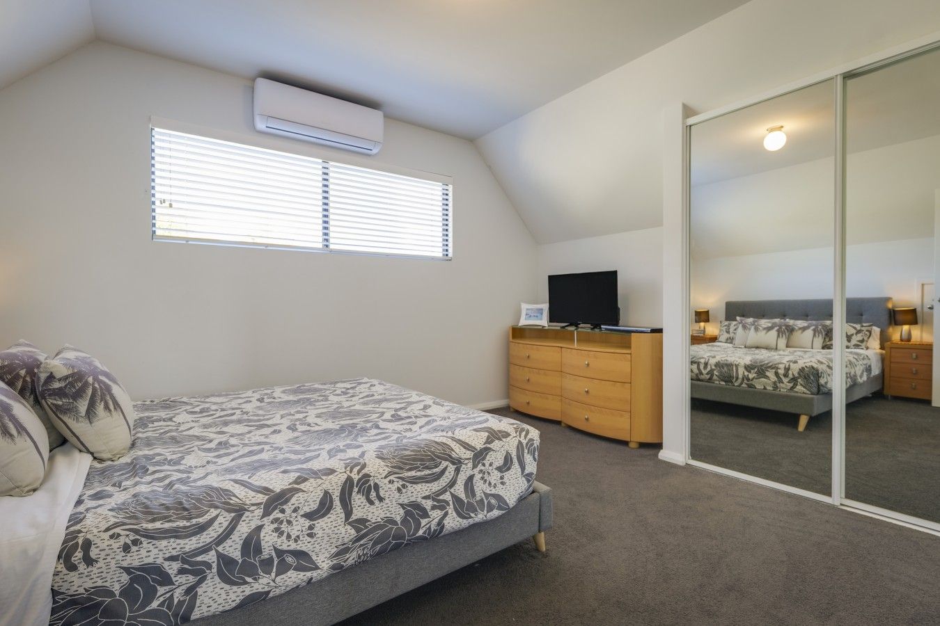 A bedroom with a bed, a dresser, a television, and a sliding glass door leading to another room.