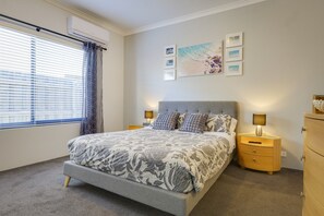 Un dormitorio con cama, dos mesitas de noche, cómoda, ventana con persianas y decoración en la pared.