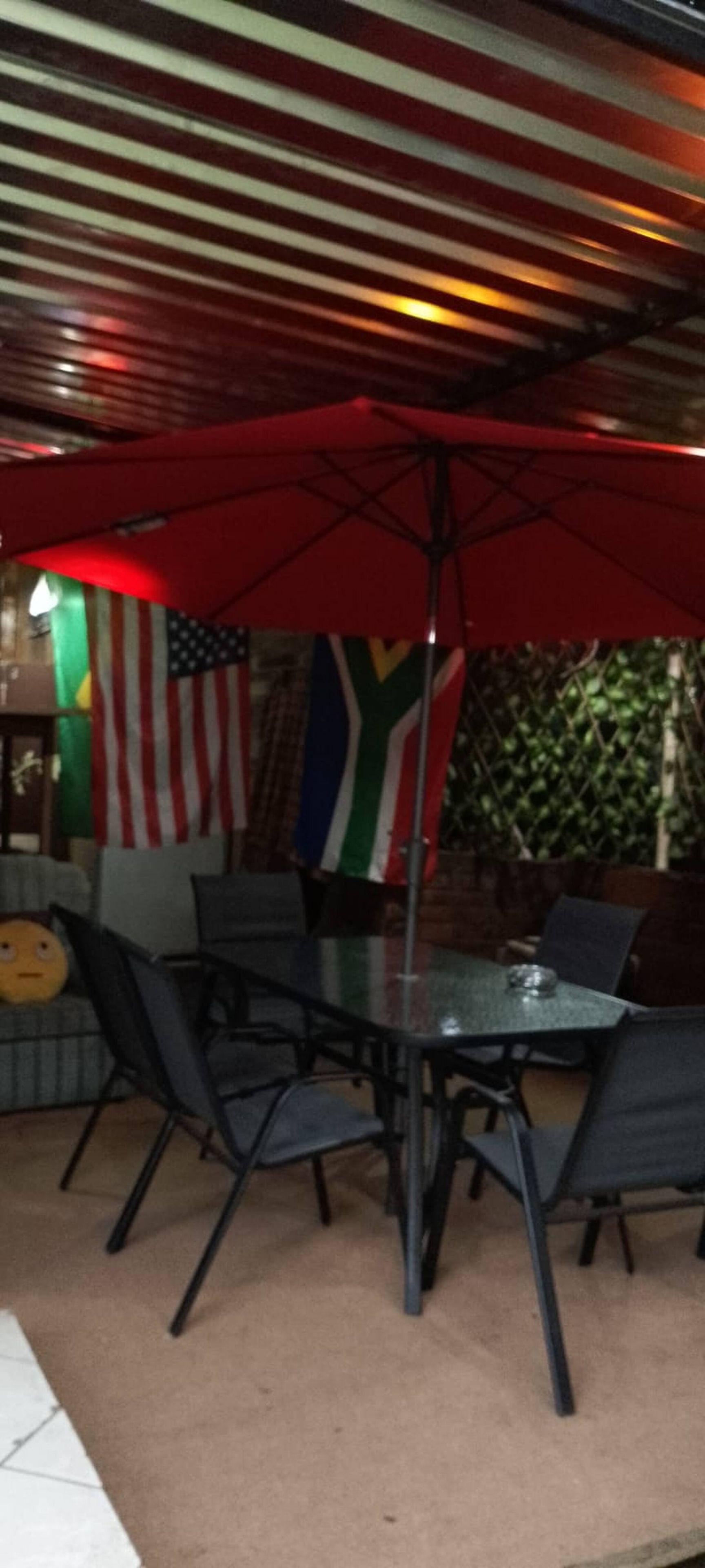 Un área de comedor al aire libre con una mesa, sillas, un paraguas rojo y banderas en la pared.