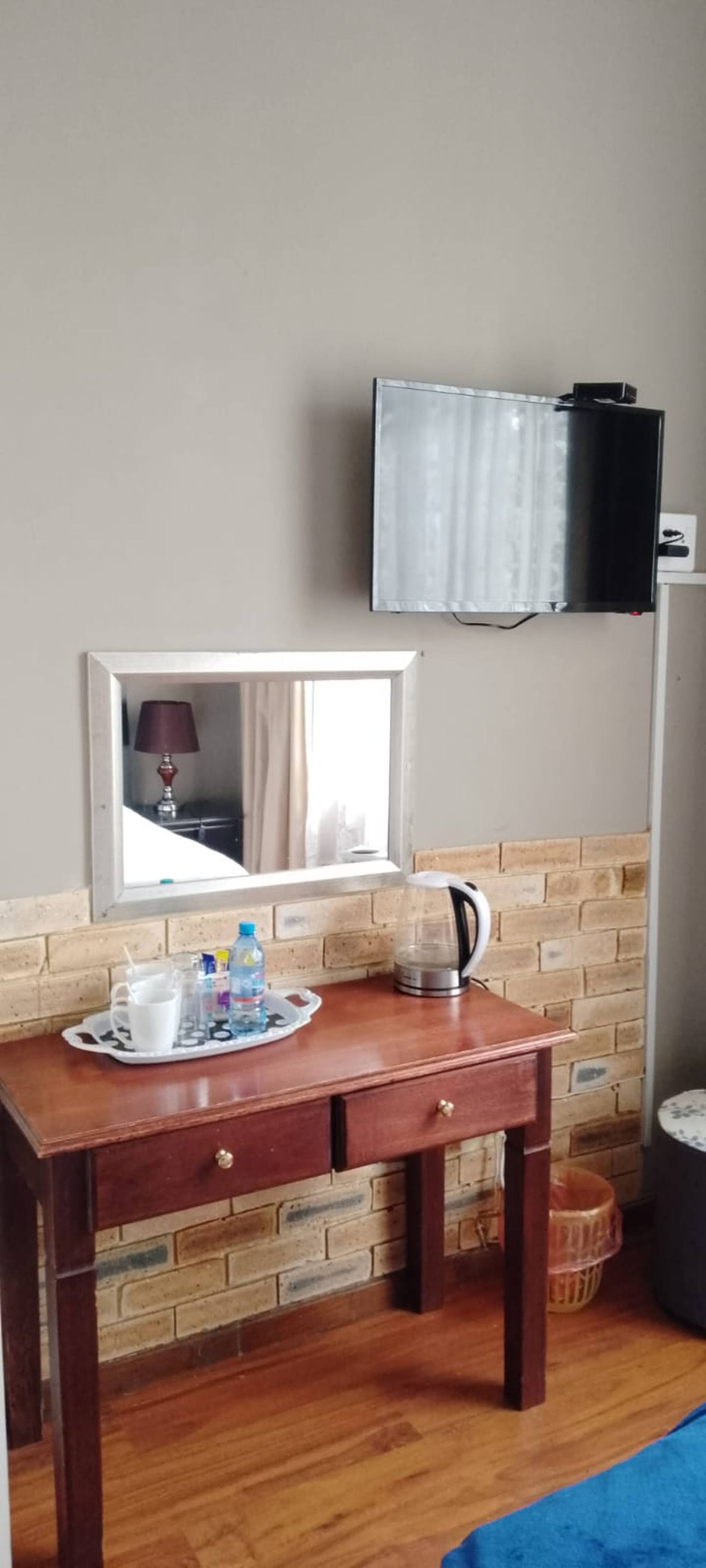 Une pièce avec un bureau en bois, un miroir, un téléviseur fixé au mur et un mur en briques.