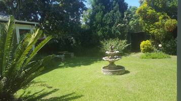 Um jardim bem cuidado com uma fonte central, cercado por vegetação exuberante e diversas árvores.