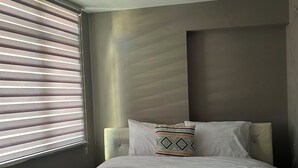 Ein Hotelzimmer mit Bett, einem Fenster mit Jalousien, einem Heizkörper und einer Lampenleuchte.