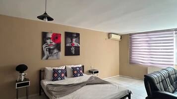 A bedroom with a bed, a nightstand, a lamp, a window with blinds, and wall art.
