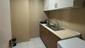 Eine kleine Küche mit weißen Schränken, einem Spülbecken, einem Wasserkocher und einem Kühlschrank.