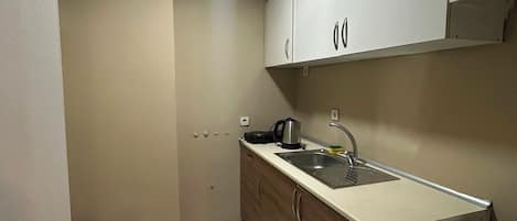 Una cocina compacta con armarios blancos, un lavabo, una tetera y un refrigerador.