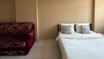 A bedroom with a bed, two pillows, a red sofa, and a ceiling light fixture.