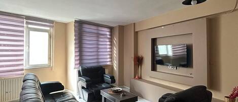 Ein Wohnzimmer mit einer Sofagarnitur, einem Couchtisch, einem an der Wand befestigten Fernseher und einem Deckenventilator.