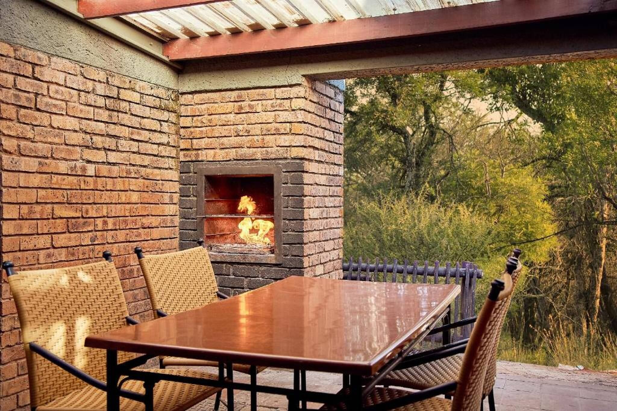 Une terrasse extérieure avec une cheminée en briques, une table en bois et des chaises en osier.