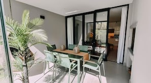 A dining area with a table and chairs, a hanging plant, and a view through a glass door to another room. - Luxury One-Bedroom with Balcony -Unit 9 (Stellenbosch)