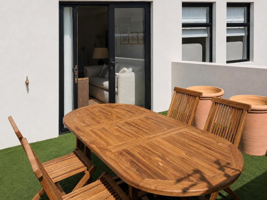 A wooden dining table with chairs, a sliding glass door, and a window with a view of a room.