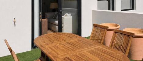 A wooden dining table with chairs, a sliding glass door, and a window with a view of a room.