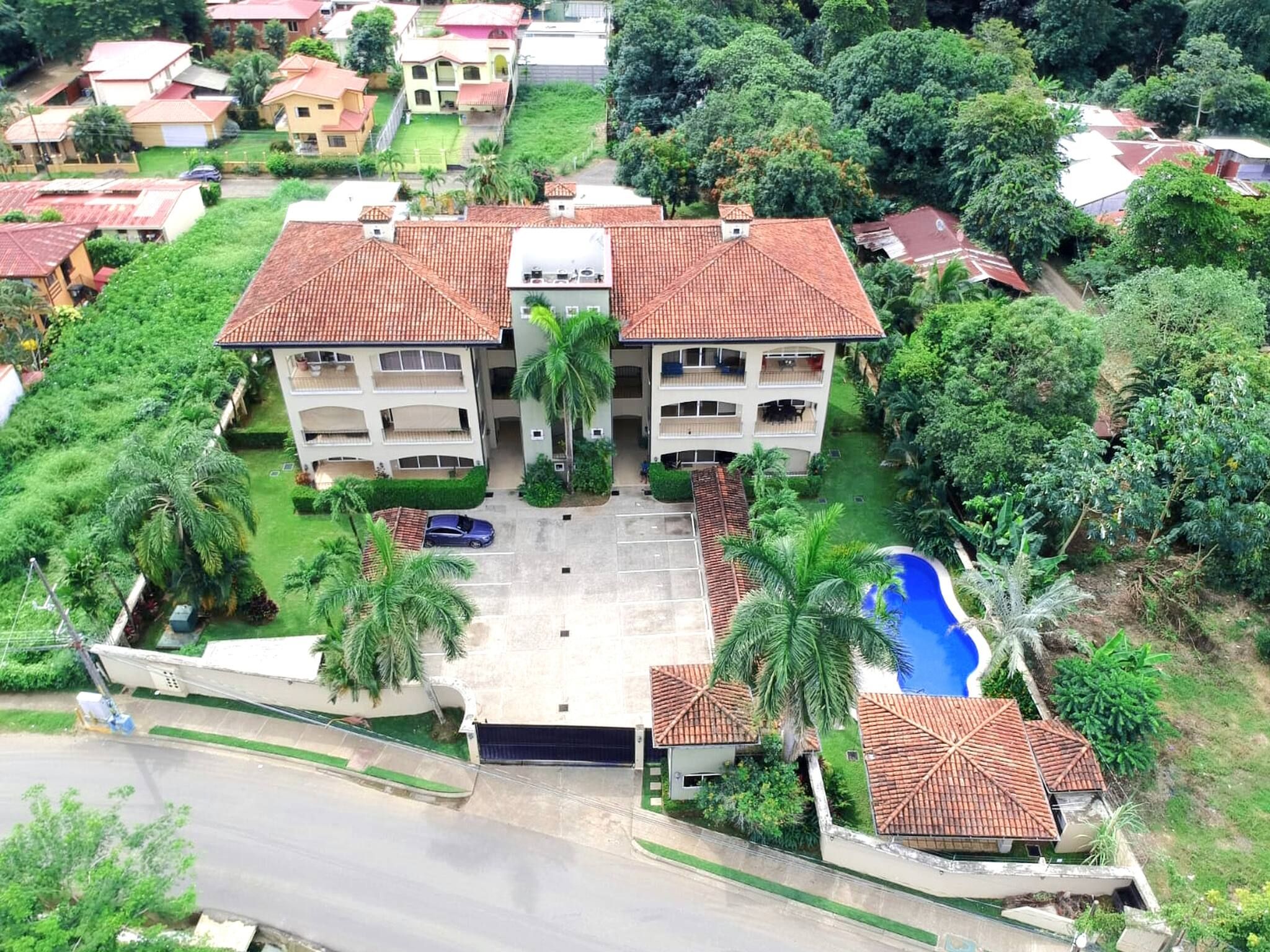 A multi-story hotel with a central courtyard, surrounded by lush greenery and a swimming pool.