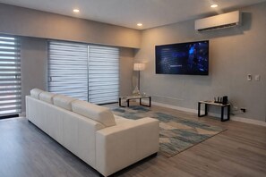 A modern living room with a sofa, a flat-screen TV, a lamp, and a small table. - Modern 3BR Condo in JacoBay - Walk to the beach 2blocks (Jaco)