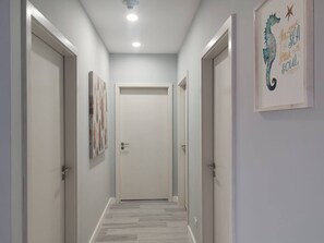 A hallway with a door at the end, flanked by two doors and a wall-mounted artwork. - Modern 3BR Condo in JacoBay - Walk to the beach 2blocks (Jaco)