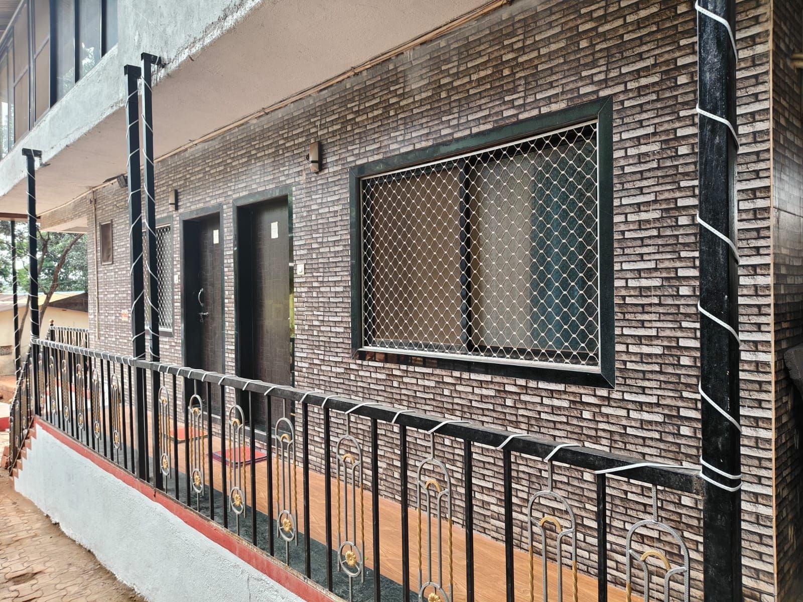 Un edificio con fachada de ladrillo, cerca metálica y un ventanal con mosquitero.