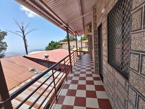 A balcony with a checkered floor, metal railing, and a view of the landscape. - Kaushik Cottage Matheran (Matheran)