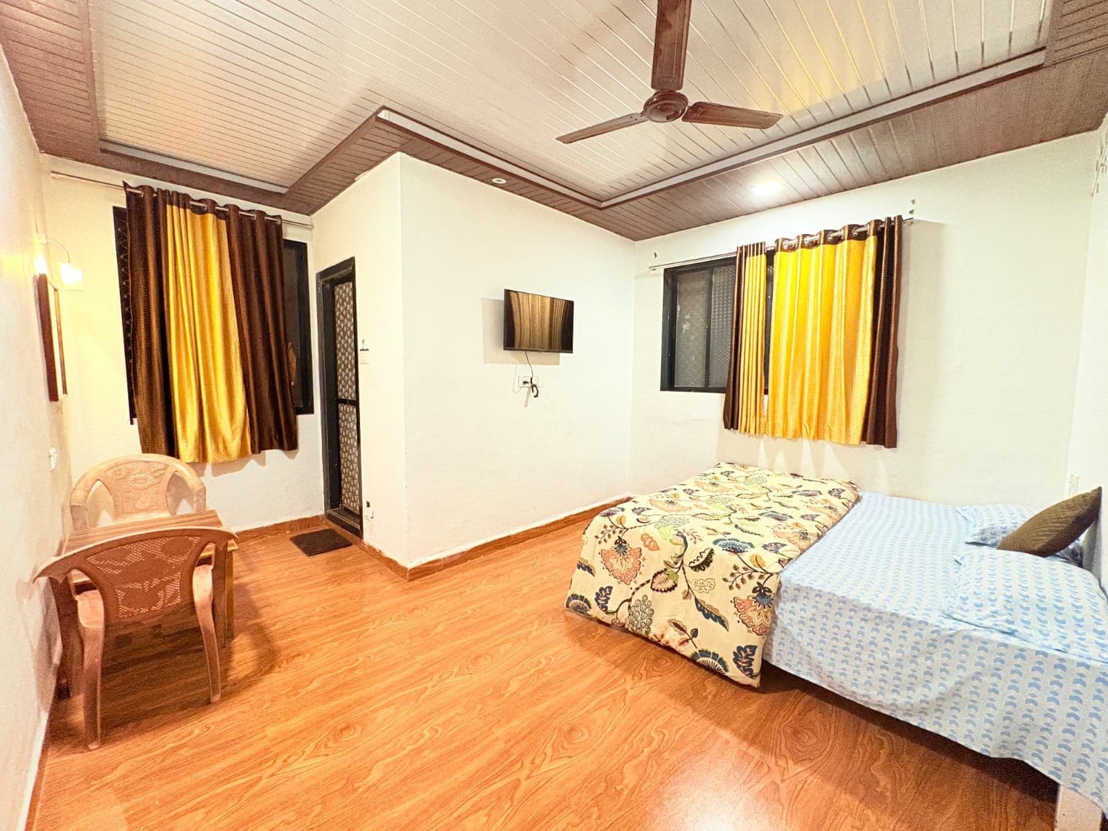 Ein Zimmer mit einem Bett, einem Sessel, einem Deckenventilator und Vorhängen.