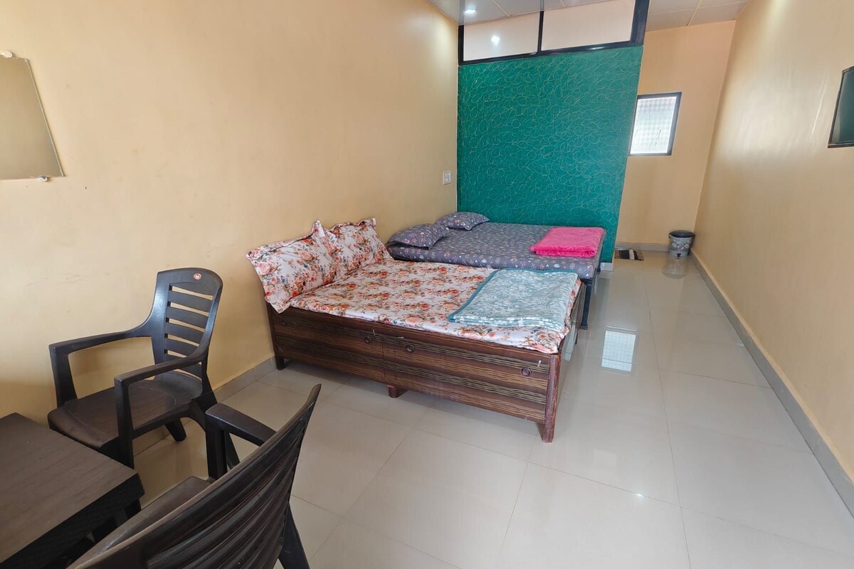 A bedroom with a bed, two chairs, a small table, and a green accent wall.