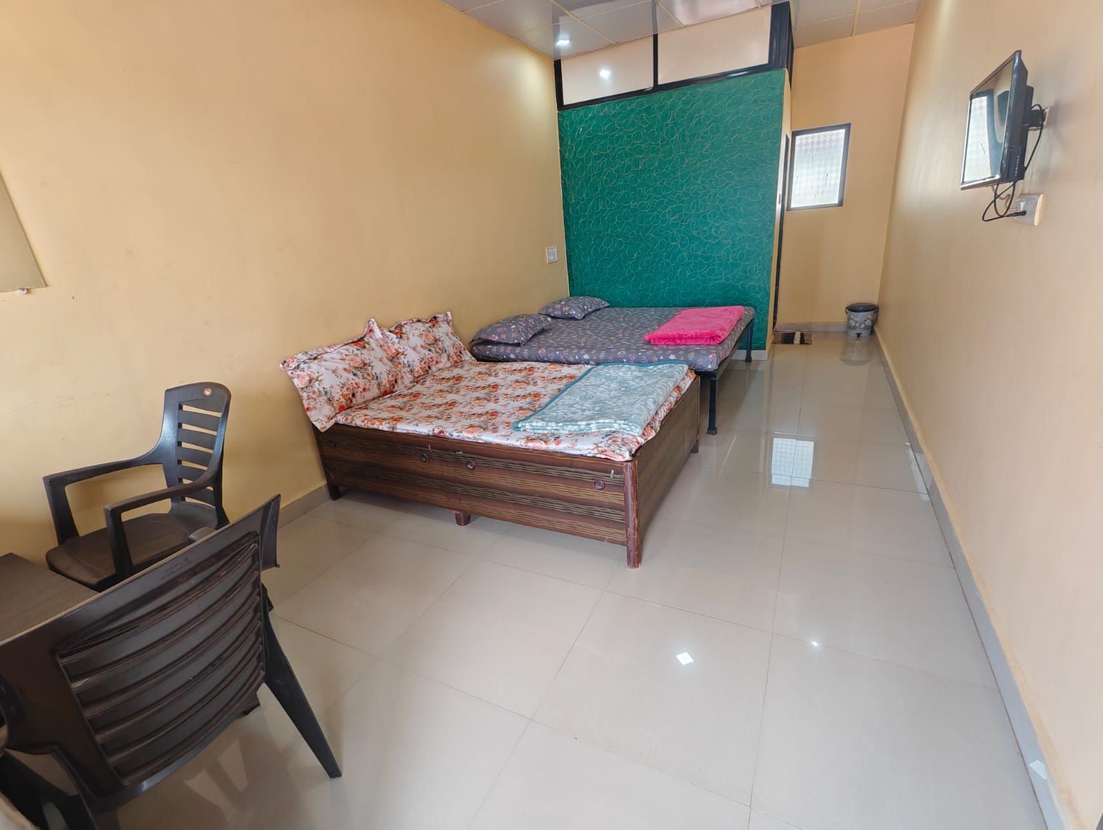 A room with a bed, a chair, a television, and a green partition wall.