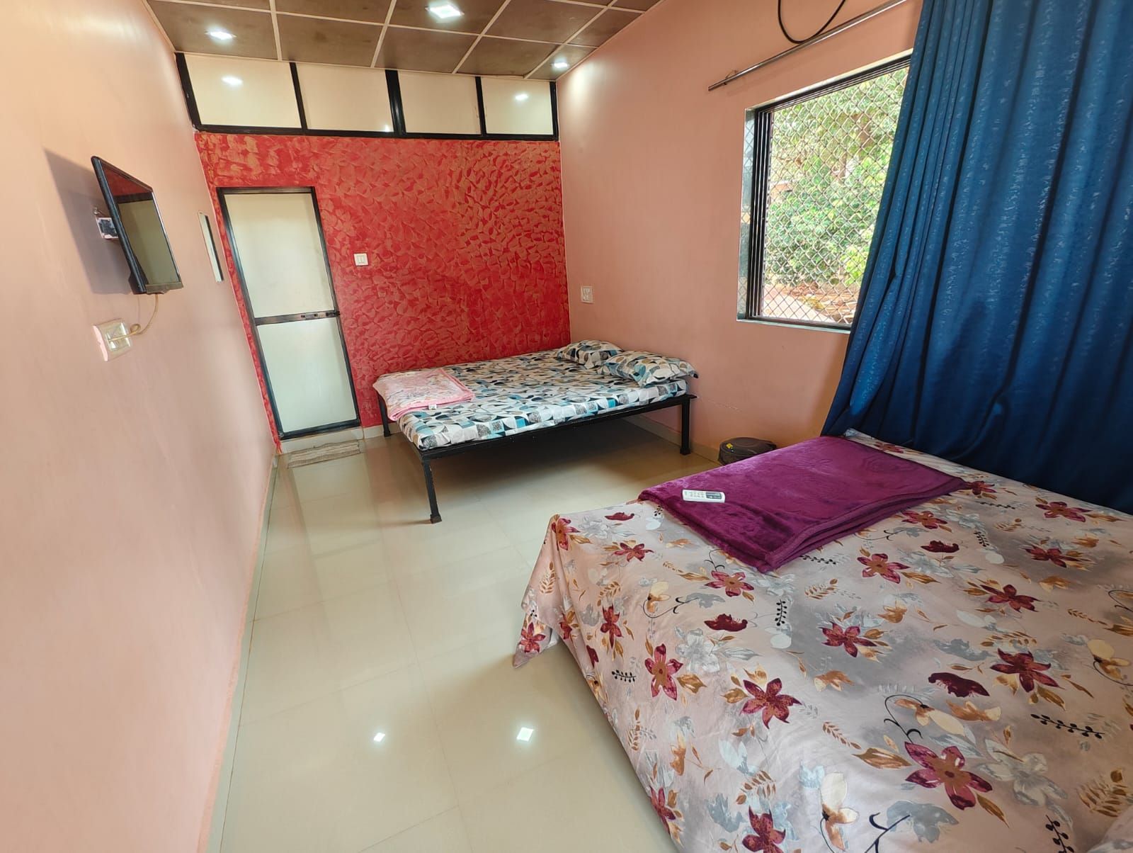 A bedroom with a bed, a window with curtains, a wall-mounted TV, and a door.