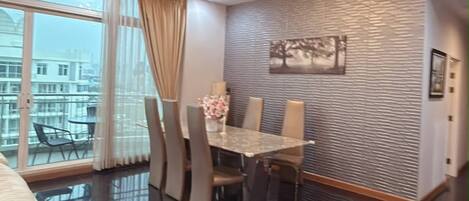 Un comedor moderno con una araña, una mesa de comedor con sillas y vistas a la ciudad a través de amplias ventanas.