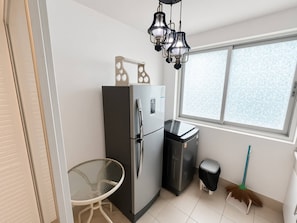 Eine kleine Küche mit Kühlschrank, Mülleimer, Besen und einem Fenster.