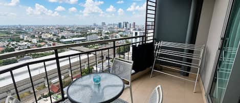 A balcony with a table and chairs, a clothes drying rack, and a view of a cityscape.