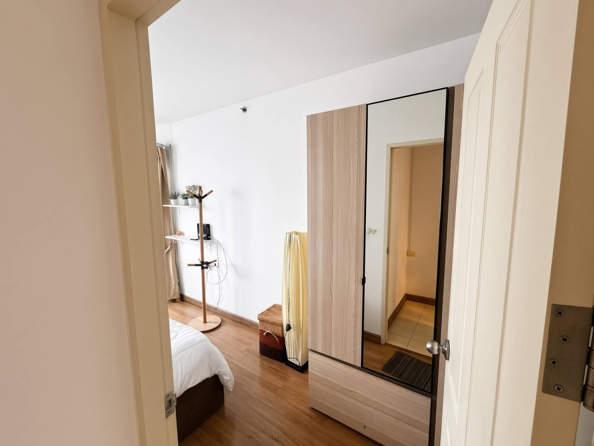 Une chambre avec un grand miroir, un lit, une armoire et un support pour plantes.