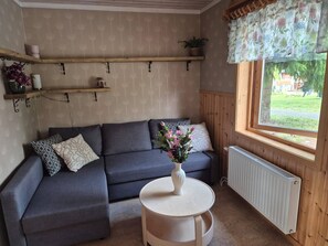 A cozy room with a grey sectional sofa, a small round table with a vase of flowers, and a window with a view of greenery.