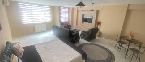 Ein modernes Wohnzimmer mit einer Couch, einem Esstisch mit Stühlen, einem an der Wand montierten Fernseher und einem Deckenventilator.
