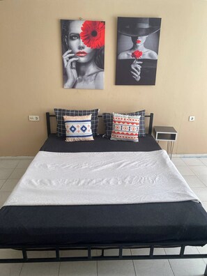 Una cama con estructura negra, ropa de cama blanca y almohadas estampadas. Dos obras de arte están colgadas en la pared sobre la cama.