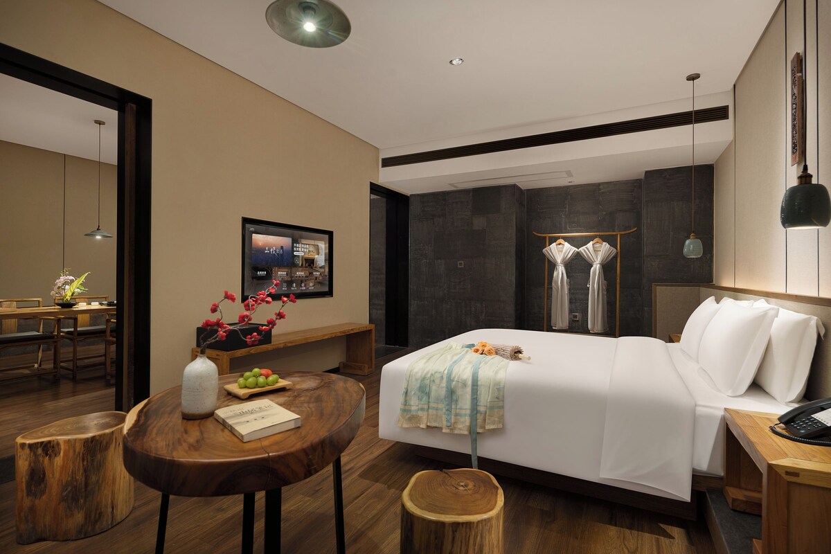 A modern hotel room with a bed, bedside table, and a desk with a chair.