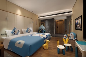 Habitación de hotel con una cama grande, un escritorio, una silla y una mesita. También hay dos taburetes pequeños y una figurita de juguete.