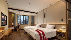 Hotellihuone, jossa on kaksi sänkyä, puinen työpöytä, pieni pöytä maljakolla ja näkymä kaupunkiin ikkunasta.