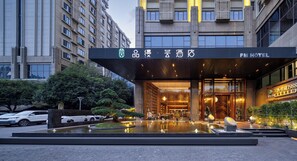 Entrada d'hotel amb un disseny modern, una fontera al davant i un senyal que indica que és un PM Hotel.