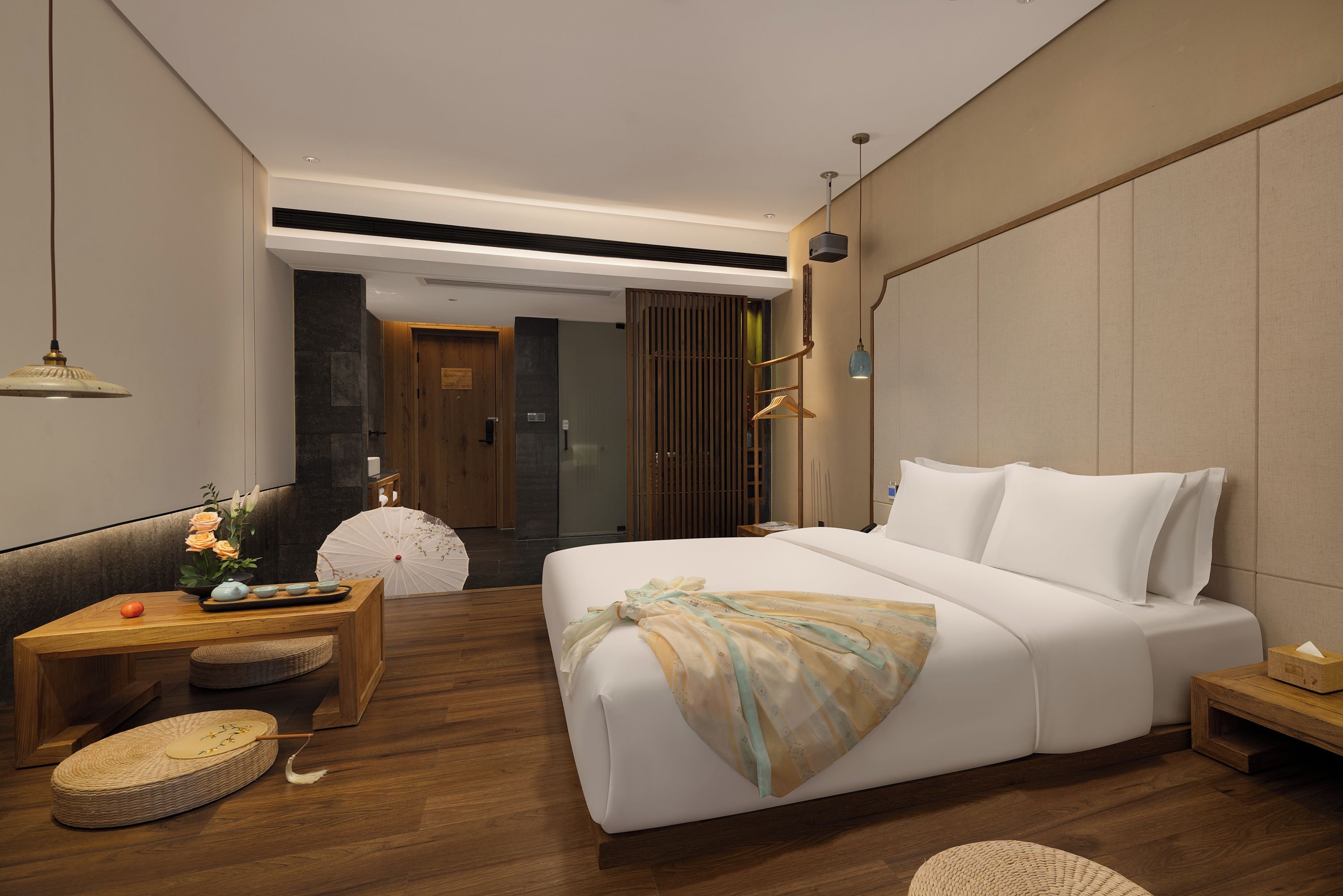 Quarto de hotel moderno com uma cama grande, uma mesinha de madeira, um pequeno espaço de estar e vista para o corredor.