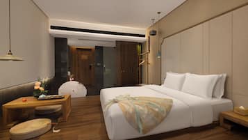 Quarto de hotel moderno com uma cama grande, uma mesinha de madeira, um pequeno espaço de estar e vista para o corredor.