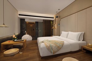 Una habitación de hotel moderna con una cama grande, una mesita de noche de madera, una pequeña zona de estar y vistas al pasillo.